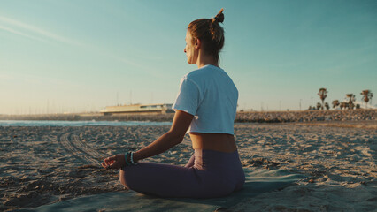 Fototapeta na wymiar Back view beautiful woman in sportswear sitting in lotus pose meditating by the sea. Female yogi practicing yoga on beach
