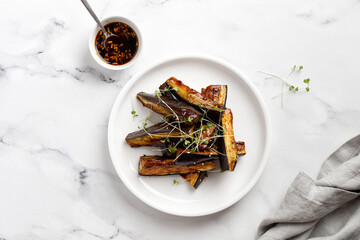 Hot spicy Glazed Fried eggplant with sauce, honey, microgreens on white plate and marble...