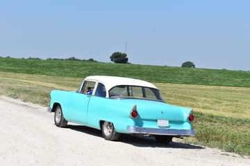 Classic Car on a Gravel Road by a Farm Field