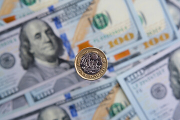 British one pound coin close up and blurred hunder dollar banknotes on the background. Concept for...