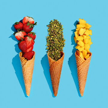 Wafer ice cream cones with fresh fruits strawberry ,maracuja, mango, peach and pistachio ,continuous pattern on blue background. Isolate top view, hard light