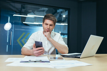 Upset and thinking man working in office, businessman looking at phone screen reading financial news from stock exchange
