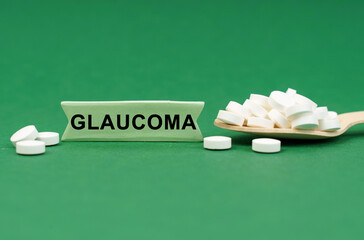 On a green surface, a wooden spoon with pills and a sign with the inscription - GLAUCOMA