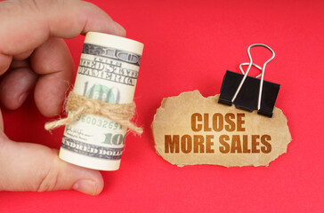 The man has dollars in his hands, on a red surface there is a cardboard sign with the inscription - Close More Sales