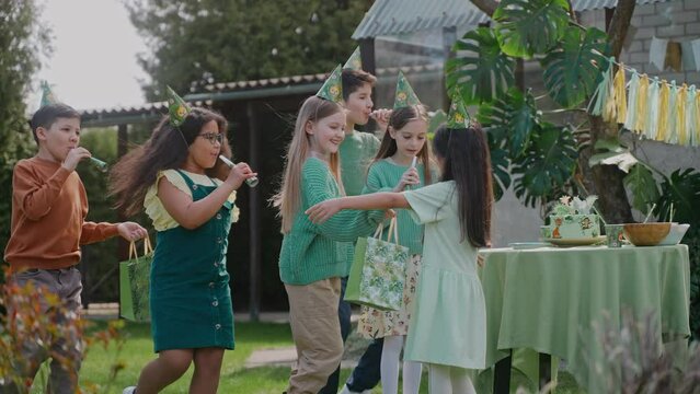 Boys and girls run up to the birthday girl at a backyard party on a sunny day. Multinational children congratulate the girl on her birthday. Green-themed birthday party. High quality 4k footage