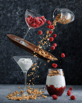 Healthy breakfast in motion with yogurt, meals, granola, raspberry and gem, in glass. Design concept on dark background