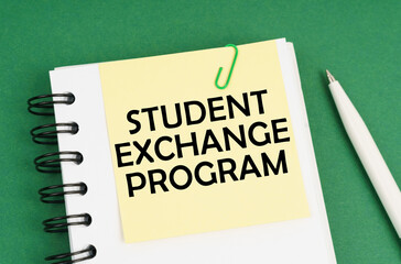 On a green surface, a pen, a notepad with stickers and the inscription - STUDENT EXCHANGE PROGRAM