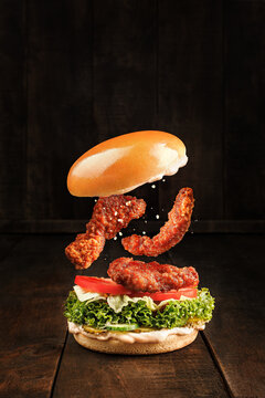 Tasty Burger with crispy chicken in motion, on rustic dark wooden background, space for text