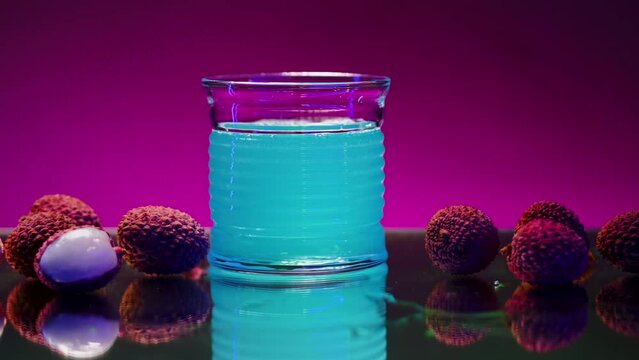 Refreshing non alcoholic beverage of blue color isolated on pink lighted wall background. Stock clip. Bar counter decorated by lychee berries.