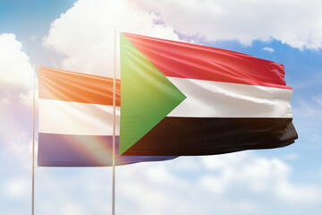 Sunny blue sky and flags of sudan and netherlands