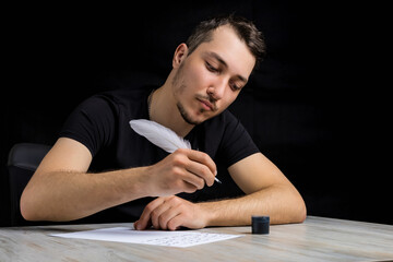 man in black clothes with a quill pen pensive looks into the distance on a black background in low...