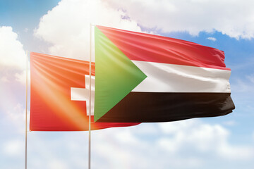 Sunny blue sky and flags of sudan and switzerland