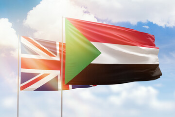Sunny blue sky and flags of sudan and united kingdom