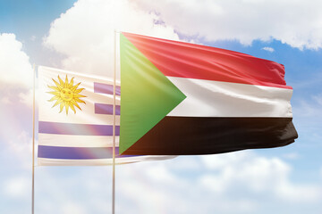 Sunny blue sky and flags of sudan and uruguay