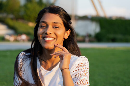 Authentic portrait of beautiful smiling Indian woman looking at camera sitting in park, copy space. Natural beauty concept
