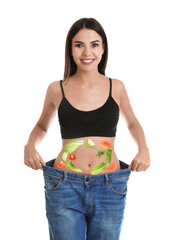 Slim young woman wearing oversized jeans and images of vegetables on her belly against white background. Healthy eating