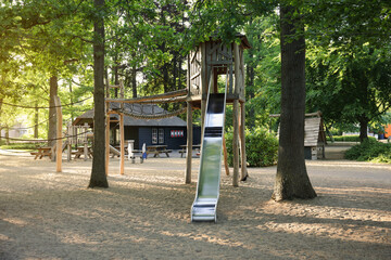 Outdoor playground with wooden slide near big trees in park