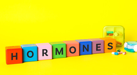 Word Hormones made of colorful cubes with letters and pills on yellow background