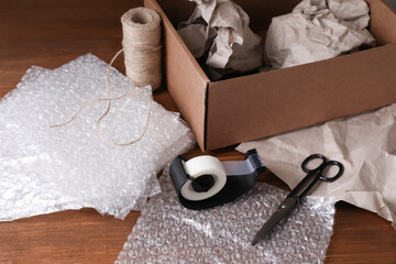 Bubble wrap, adhesive tape, twine and scissors near cardboard box on wooden table