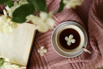 Obraz na płótnie Canvas Cup of aromatic tea with beautiful jasmine flower and open book on pink fabric, flat lay