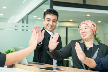 Happy business co workers giving high five to one another in office. Symbol of unity, teamwork or victory.