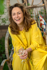 Fototapeta premium a girl in a yellow dress drinks a drink from a glass on vacation in an armchair in the garden