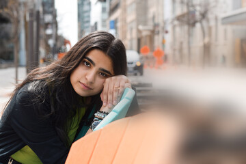 Portrait of young girl sitting on city street resting her head looking at camera