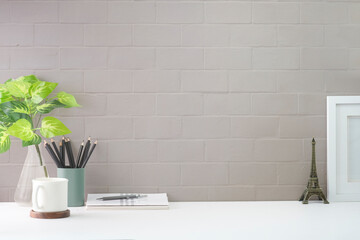 Stylish workplace with coffee cup, book, pencil holder and potted plant on white table. Copy space for your text.