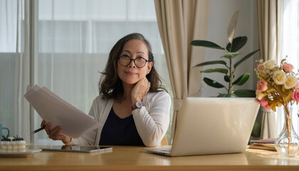 Thoughtful senior mature woman watching business training, online webinar on laptop computer while remote working from home.