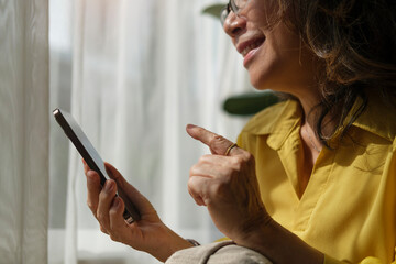 Happy middle aged woman resting on comfortable couch in bright living room and using smart phone.