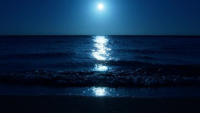 Moonlight over ocean waves washing beach sand. Full moon glowing with lunar path at water surface. Full moon glow over ocean waves on sand beach at night. Waves washing up sand beach. Dark background