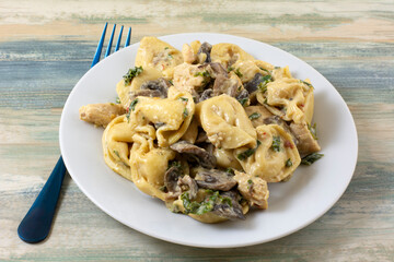 Pasta dinner with kale, mushrooms, shallot and tortellini  on white plate with blue fork