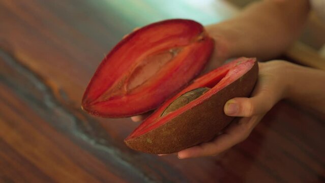 Close up shot of woman hand holding cut Zapote in Mexico. Tropical ripe fruit sapote sliced. Pouteria sapota. Guatemala.