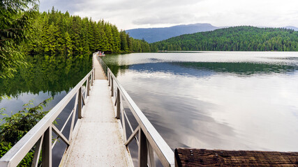 Metal footbridge across lovely BC lake to forest trail,  encompassing fishing platform in distance.