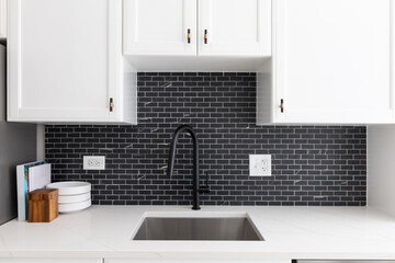 Kitchen sink detail shot with white cabinets, small black marble subway tile backsplash, and a...