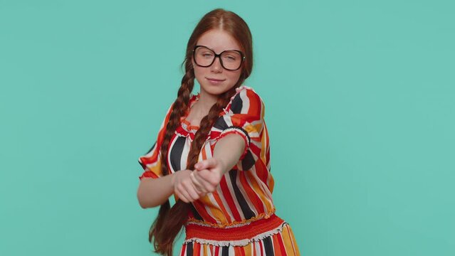 Mime redhead girl pulling an imaginary unreal invisible rope, puts lot of effort into showing how enduring, strong he is. Young ginger teenager child isolated alone on blue studio wall background