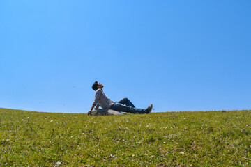 Guy sitting looking upward relaxing hands backward in green grassland and blue sky