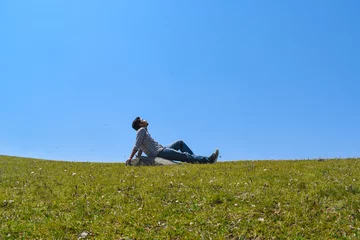 Foto op Canvas Guy sitting looking upward relaxing hands backward in green grassland and blue sky © Navaashay