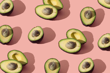 Avocado healthy food. Cut in half. Pastel pink background. Dark shadows. Modern pattern.