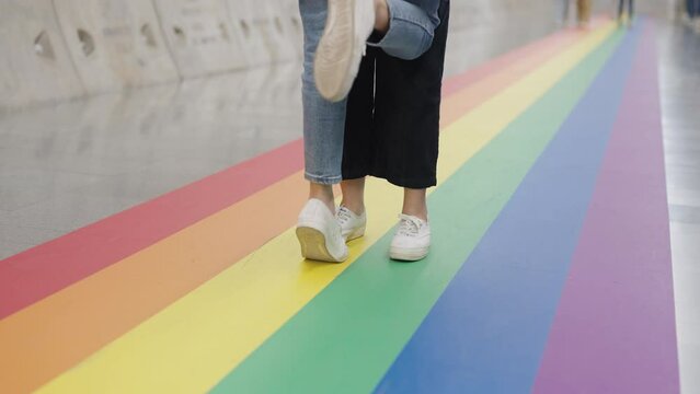 Closeup jeans foot leg white sneaker shoe queer transgender two people steps walk tiptoe kiss life go on colorful stripes flag line city street way. LGBT LGBTQIA gay color sign bisexual festival.