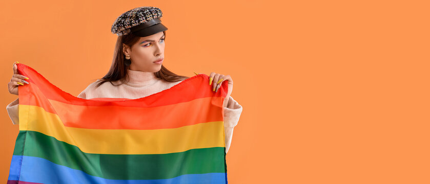 Portrait of stylish young transgender woman holding LGBT flag on orange background with space for text