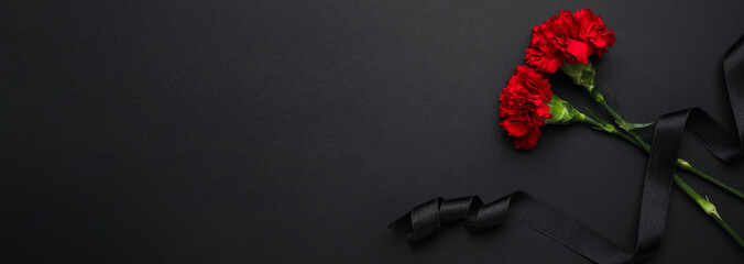 Black funeral ribbon and carnation flowers on dark background with space for text