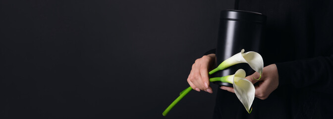 Woman holding mortuary urn and flowers on black background with space for text, closeup