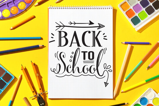 Notebook with text BACK TO SCHOOL and stationery on yellow background