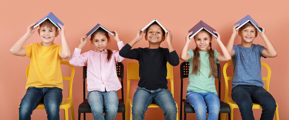 Cute little children with books sitting near color wall