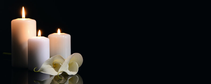 Burning candles and flowers on black background with space for text. Funeral concept
