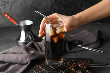 Woman holding glass of cold brew coffee on dark background