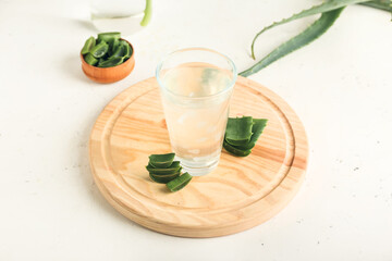 Board with glass of aloe juice and leaves on white background