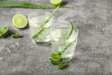Glasses of aloe juice and leaves on grunge background