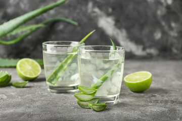 Glasses of aloe juice and leaves on grunge background